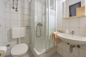 Een moderne badkamer met een glazen douchecabine, toilet en een wastafel met spiegel erboven.