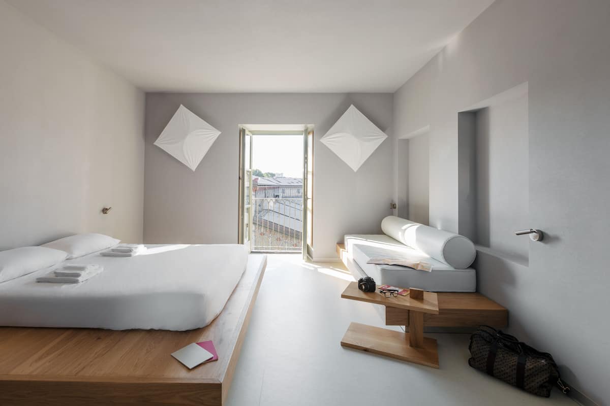 Une chambre d’hôtel moderne avec un grand lit, un canapé, un banc en bois et un bureau.