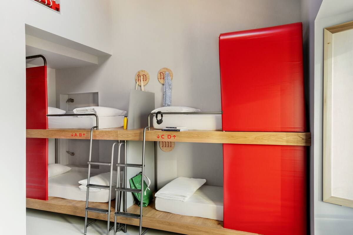 Une chambre avec un lit superposé, une échelle, un sac vert et deux crochets en bois fixés au mur.