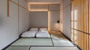 A traditional Japanese room with tatami flooring, a low bed with white bedding, and a sliding wooden door. - Combo Torino - Hostel (Turin)