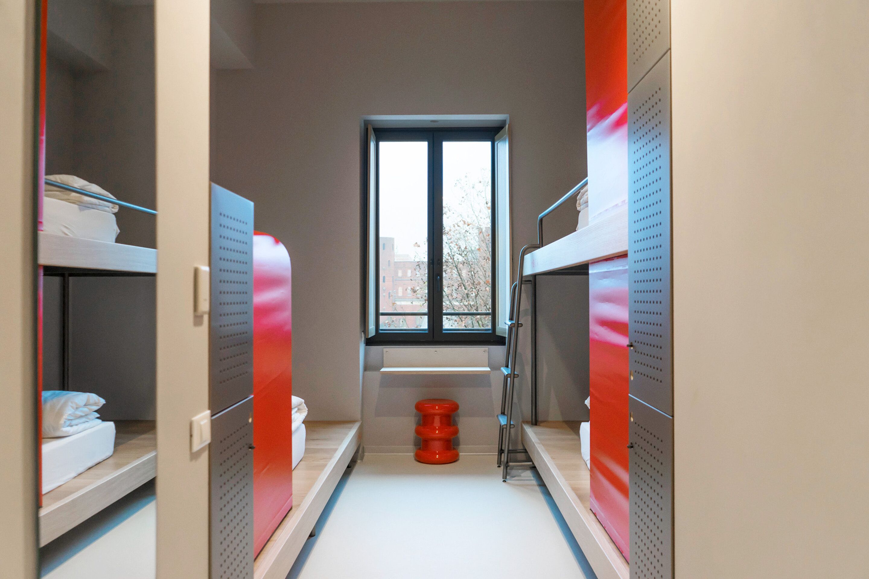 A narrow corridor with bunk beds, a window, and a red stool.