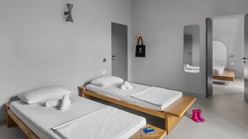 A modern hotel room with two single beds, a wooden bench, a small table, a mirror, and a wall-mounted bag rack.