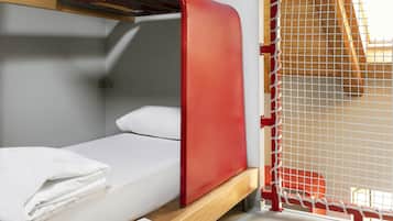 Un letto a castello con struttura rossa e biancheria bianca, un tavolino con un libro e una finestra con travi in legno.