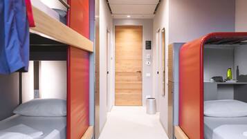 A corridor with bunk beds on either side, a wooden door at the end, and a trash bin in the middle.