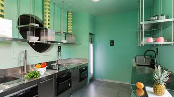 Una cocina moderna con electrodomésticos de acero inoxidable, una pared verde y un frutero en la encimera.