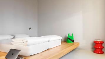 Quarto moderno com cama, um laptop, uma bolsa verde e um banquinho vermelho.