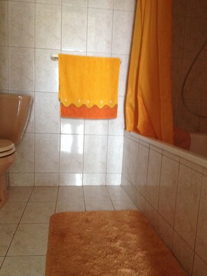A bathroom with a toilet, a towel rack with a yellow towel, a bathtub with a yellow shower curtain, and a brown rug on the floor. - Cozy apartment Nena in Medulin (Medulin)