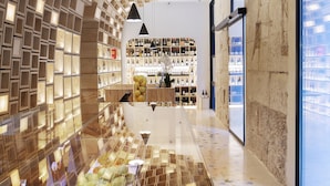 A modern interior with a unique geometric ceiling design, a long counter with various items, and a view through large windows. - Hotel Serawa Alicante (Alicante)