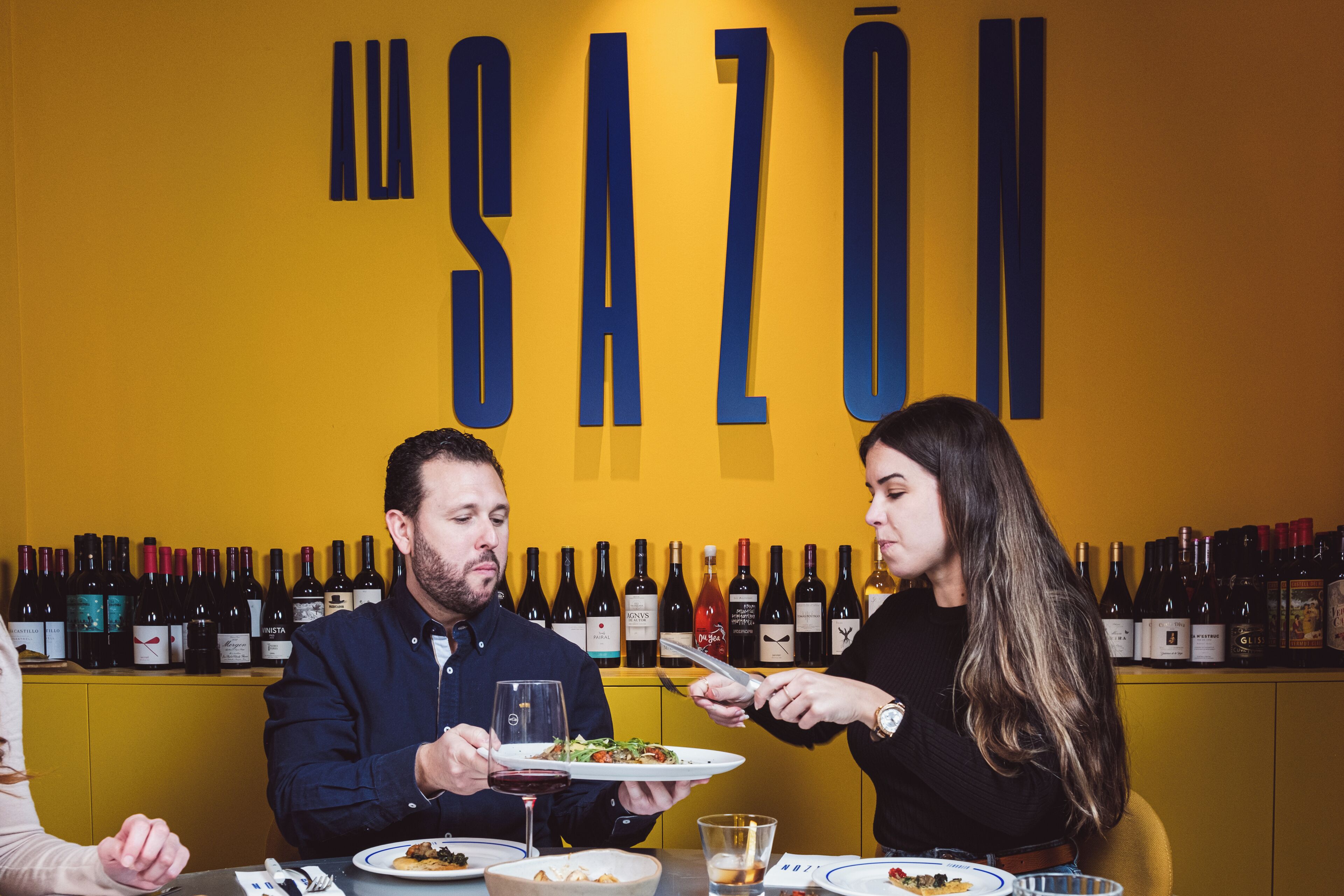 A restaurant interior with a yellow wall and a wine rack displaying various bottles.