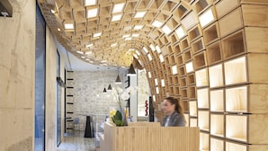 A reception area with a wooden reception desk, a stone wall, and a geometric patterned floor. - Hotel Serawa Alicante (Alicante)