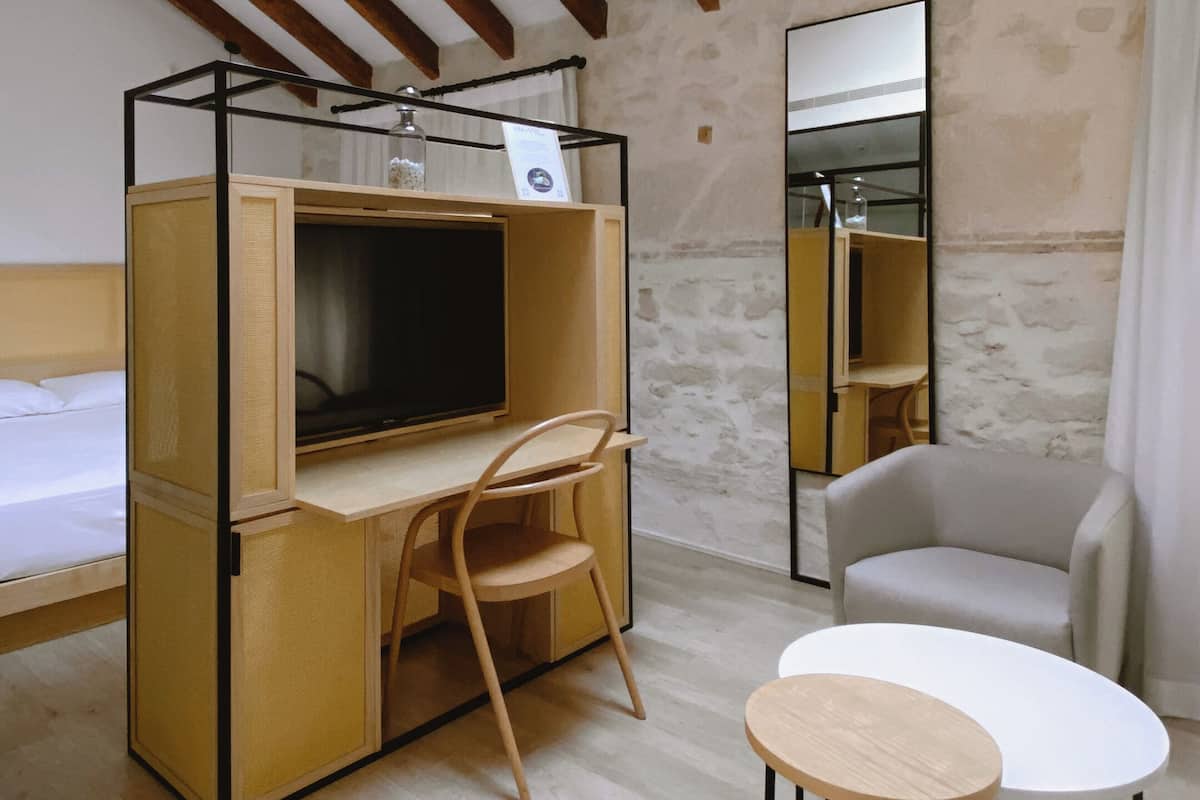 Een kleine kamer met dakraam, een bed, een bureau met stoel, een klein rond tafeltje en een spiegel.