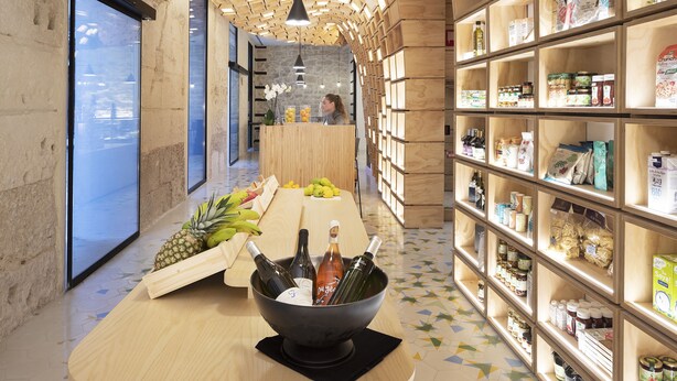 A modern interior with a wooden ceiling, a central table with bottles and fruits, and shelves with food items. - Hotel Serawa Alicante (Alicante)