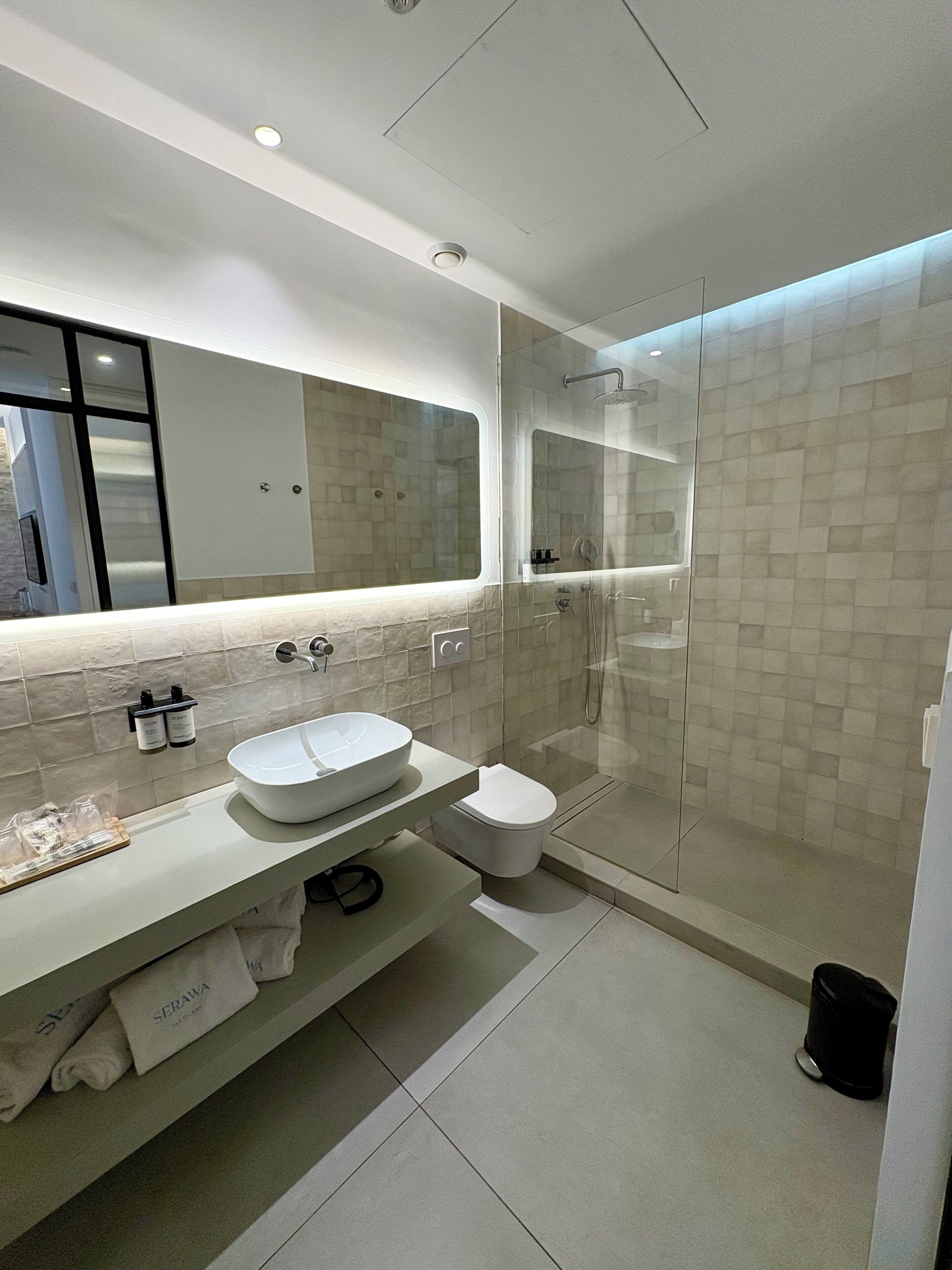 Un baño moderno con un espejo grande, un lavamanos y una ducha con cerramiento de vidrio.