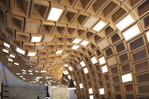 Experience the unique ceiling design with interlocking panels and pendant lights, set against a textured stone backdrop.