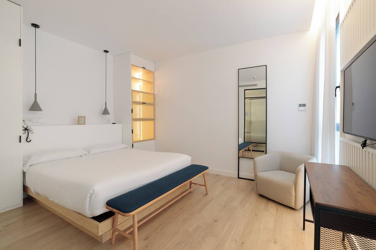 Een moderne hotelkamer met een groot bed, nachtkastje, bankje en een televisie.