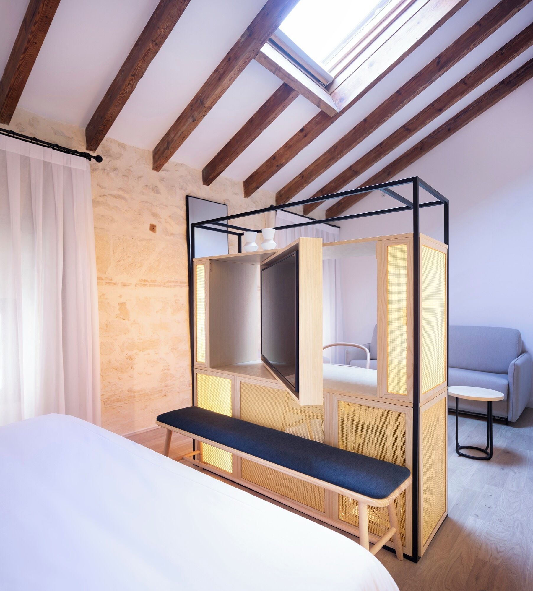 A room with a bed, a bench, a sofa, a TV, and a skylight.
