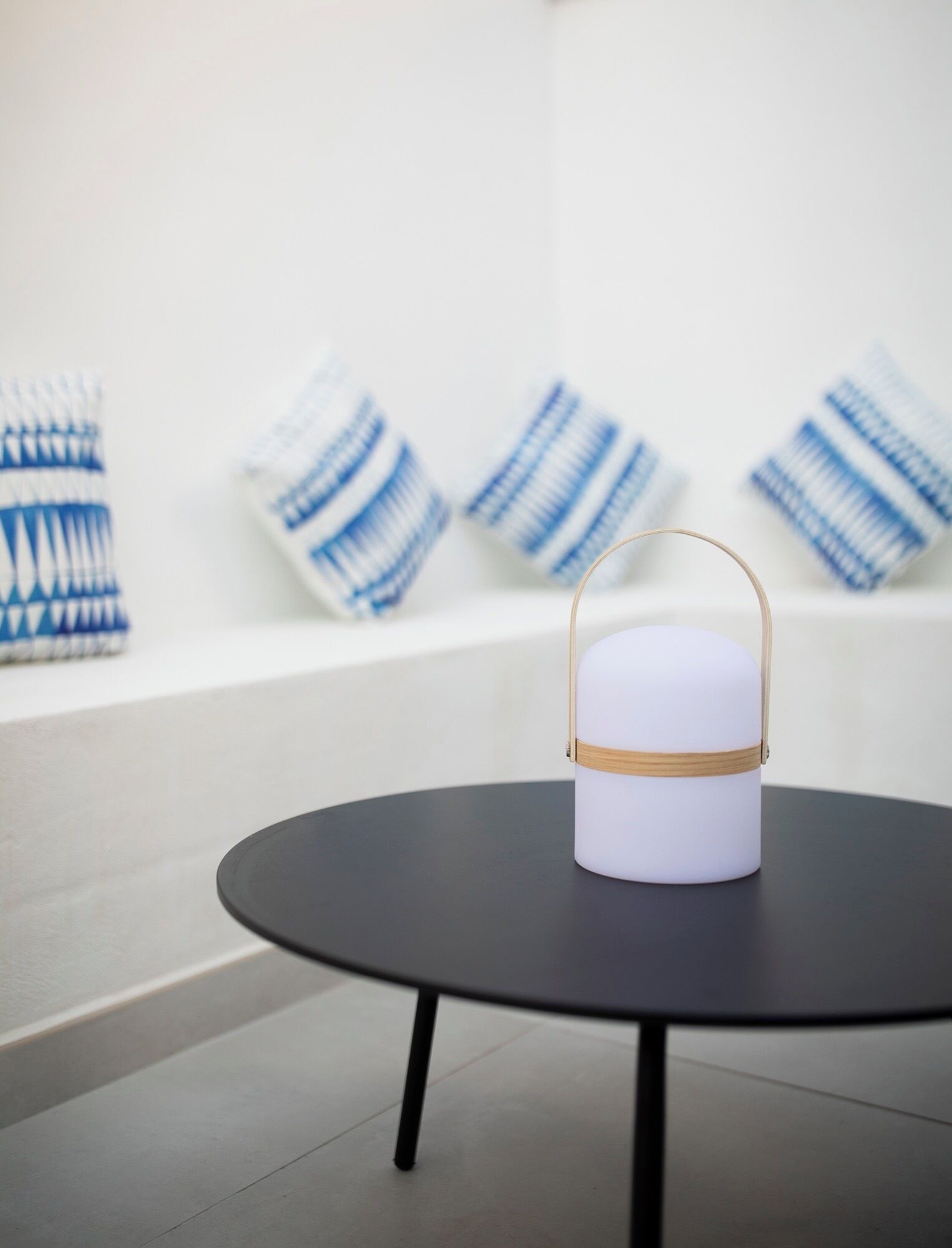 A white cylindrical object with a wooden band on a black table in a modern room with white walls and blue patterned cushions.