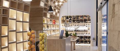 A modern interior with a geometric ceiling design, wooden reception desk, and a wine display.