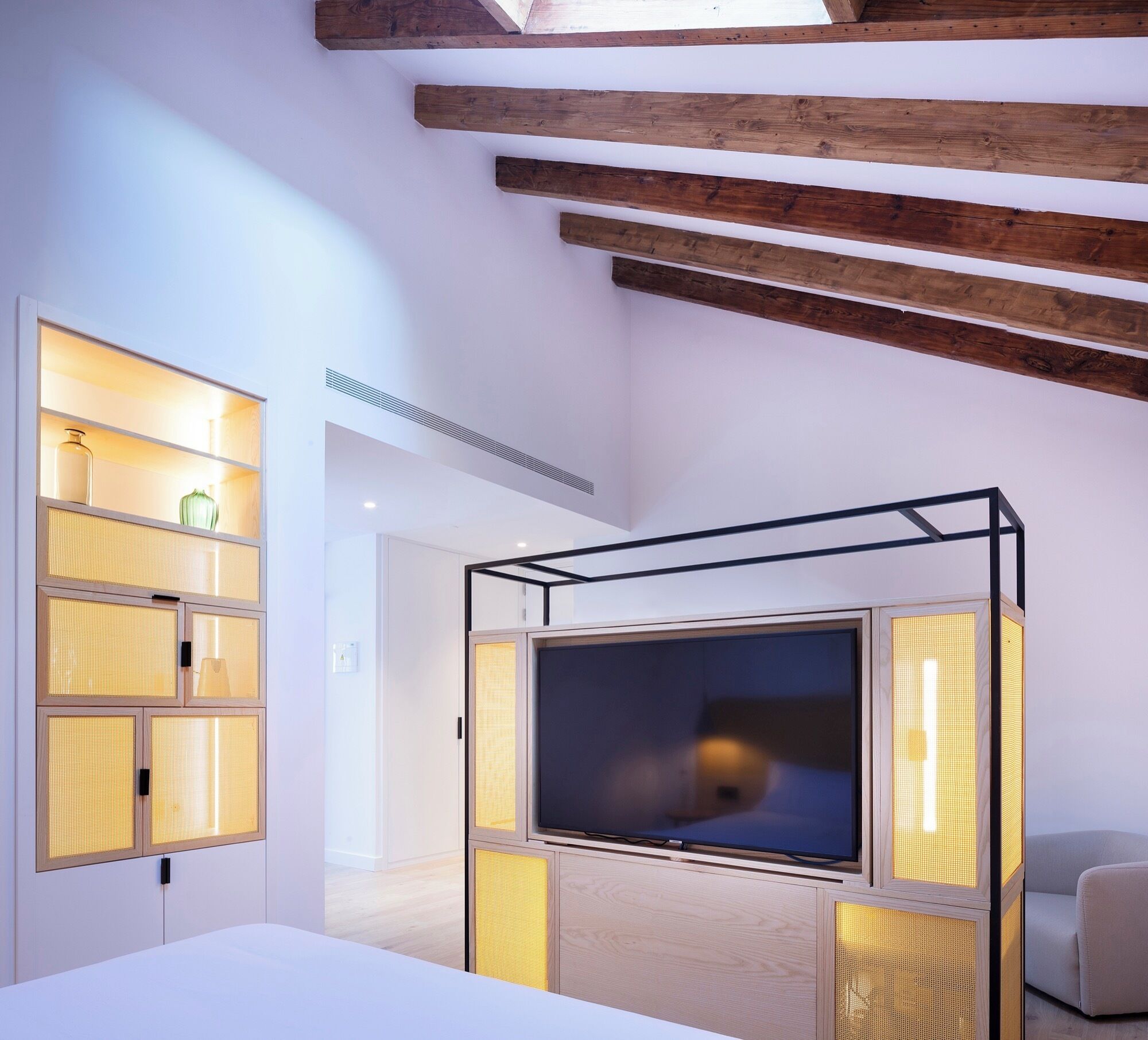 A modern bedroom with a large TV, built-in shelving, and a sloped ceiling with exposed beams.