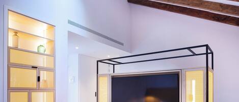 A modern bedroom with a large TV, built-in shelving, and a sloped ceiling with exposed beams.