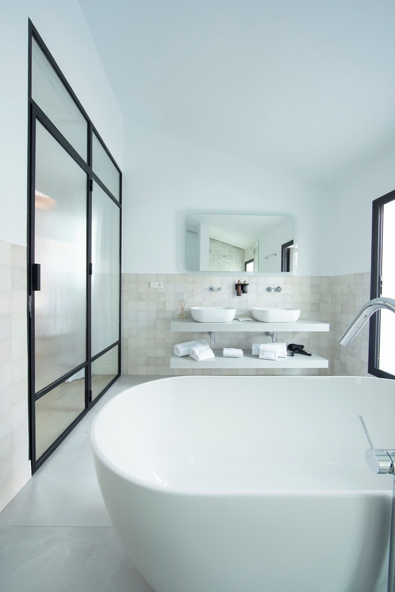 A modern bathroom with a freestanding bathtub, a large mirror, and two sinks.