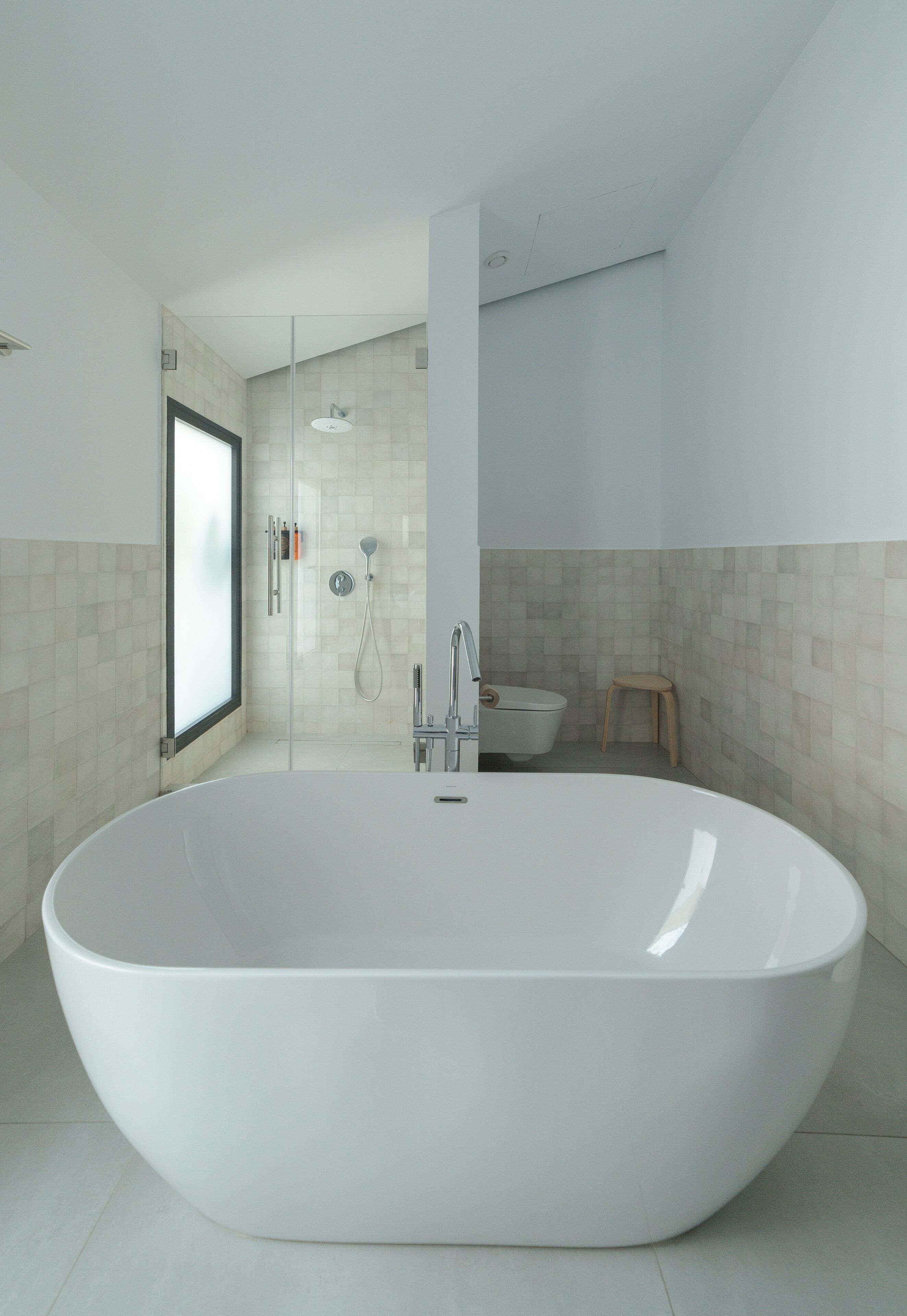Un baño moderno con una bañera independiente grande, zona de ducha con mampara de vidrio y un inodoro.