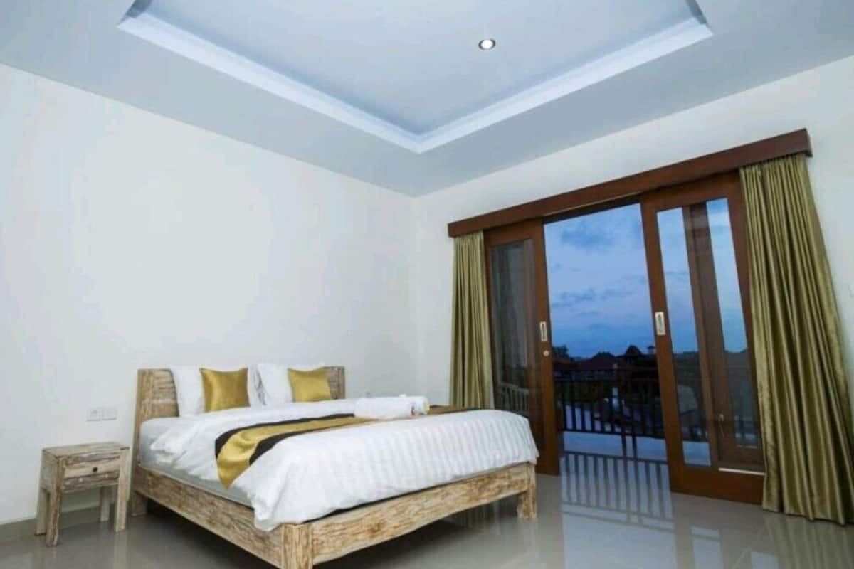 A bedroom with a large bed, a nightstand, a ceiling light, and a sliding glass door leading to a balcony.