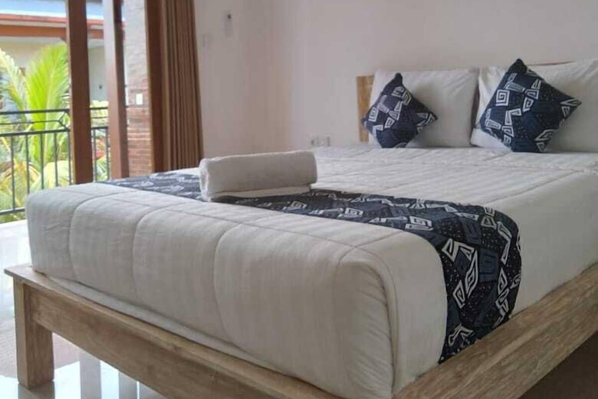 A bedroom with a bed, pillows, a painting, and a balcony.