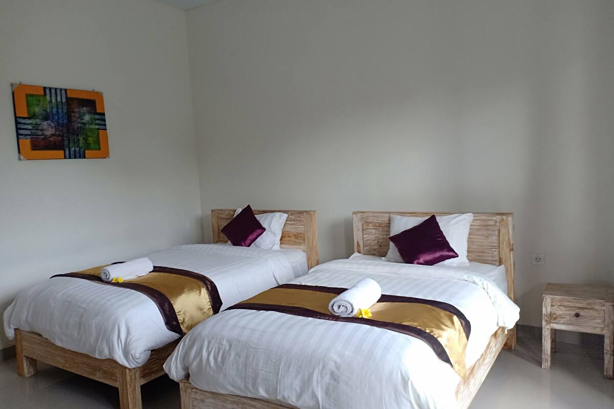 A hotel room with two wooden beds, white bedding, and a small bedside table.