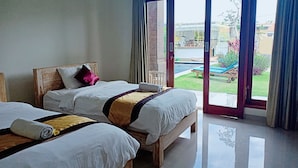 A hotel room with two beds, a balcony with a view of a swimming pool and garden, and a sliding glass door. - Bali Billy Village (Canggu)
