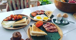 A breakfast spread on a table with toast, eggs, tomatoes, and bacon. - Bali Billy Village (Canggu)