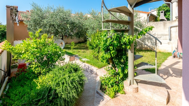 A courtyard with a tiled pathway, green plants, and a metal spiral staircase. - Affordable Apartment Bruno in Pula (Pula)
