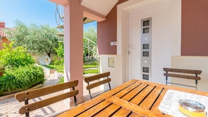 A wooden table with benches in a covered outdoor area with a view of greenery and a building in the background. - Affordable Apartment Bruno in Pula (Pula)