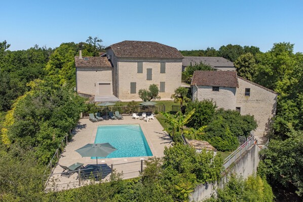 A stone building with a swimming pool, surrounded by lush greenery.