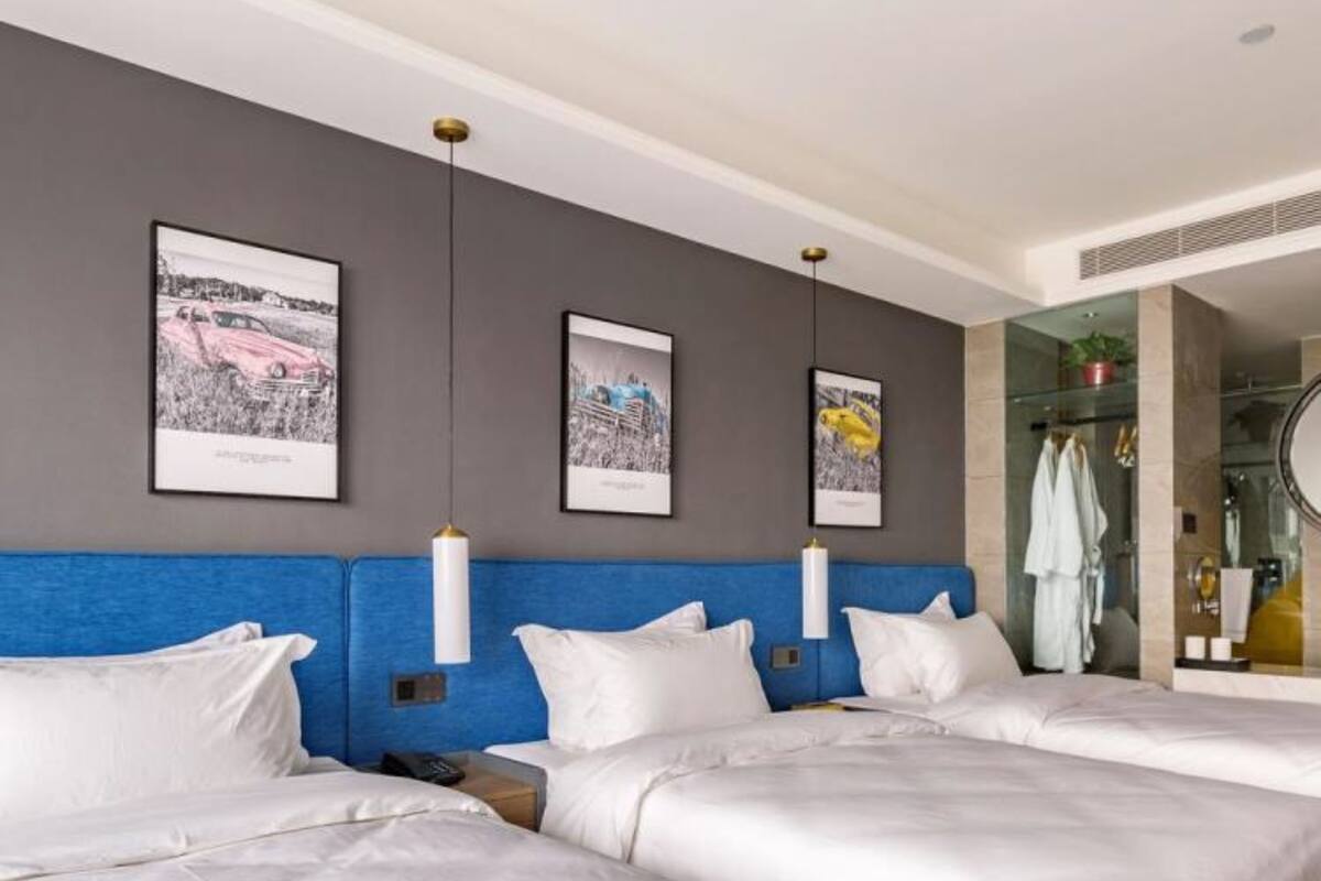 A hotel room with two beds, a grey accent wall, and three framed pictures.
