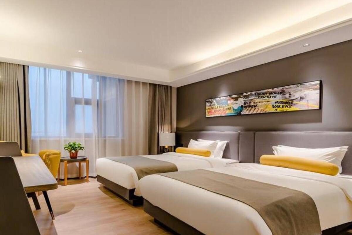 A hotel room with two beds, a desk, and a large window with curtains.