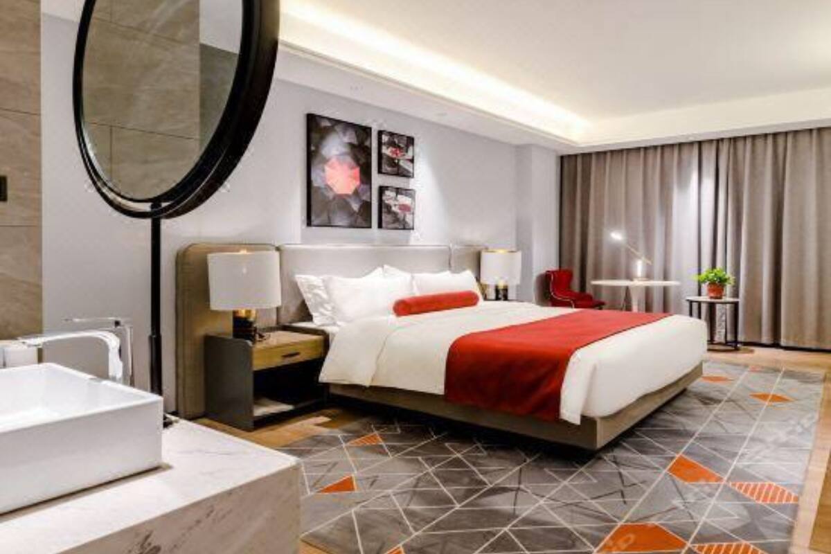 A hotel room with a bed, bedside tables, a mirror, a bathroom with a sink, and a patterned rug.