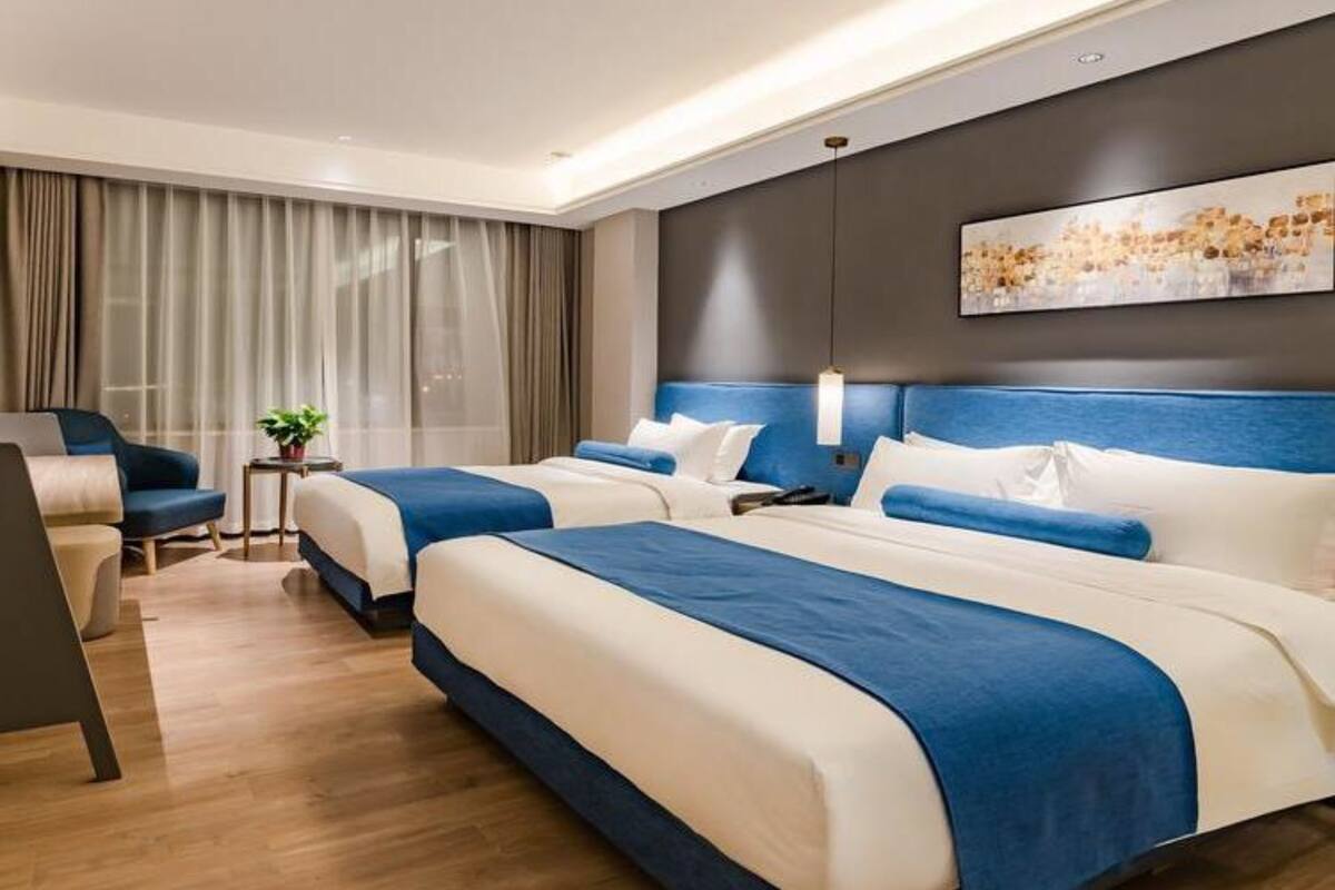 A modern hotel room with two beds, a seating area, and a cityscape painting on the wall.