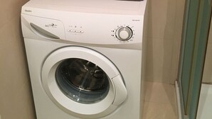 Un lave-linge à chargement frontal doté d’un panneau de commande et d’une étagère rouge située au-dessus, sur laquelle sont pliées des serviettes.