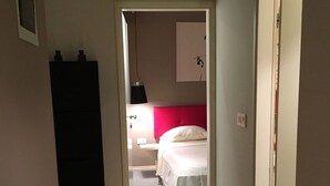 Un couloir étroit mène à une chambre à coucher qui contient un lit, une table de chevet et une lampe.