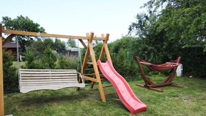 A wooden swing set with a red slide in a grassy backyard.