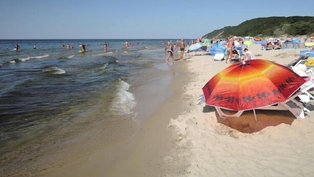 A beach with clear water, people swimming, and beach umbrellas.