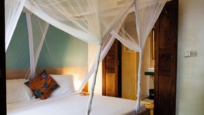 A bed with a canopy, a colorful pillow, and a wooden headboard. - Pili Pili House (Jambiani)
