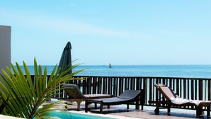 A poolside area with lounge chairs and an umbrella, overlooking the sea. - Pili Pili House (Jambiani)