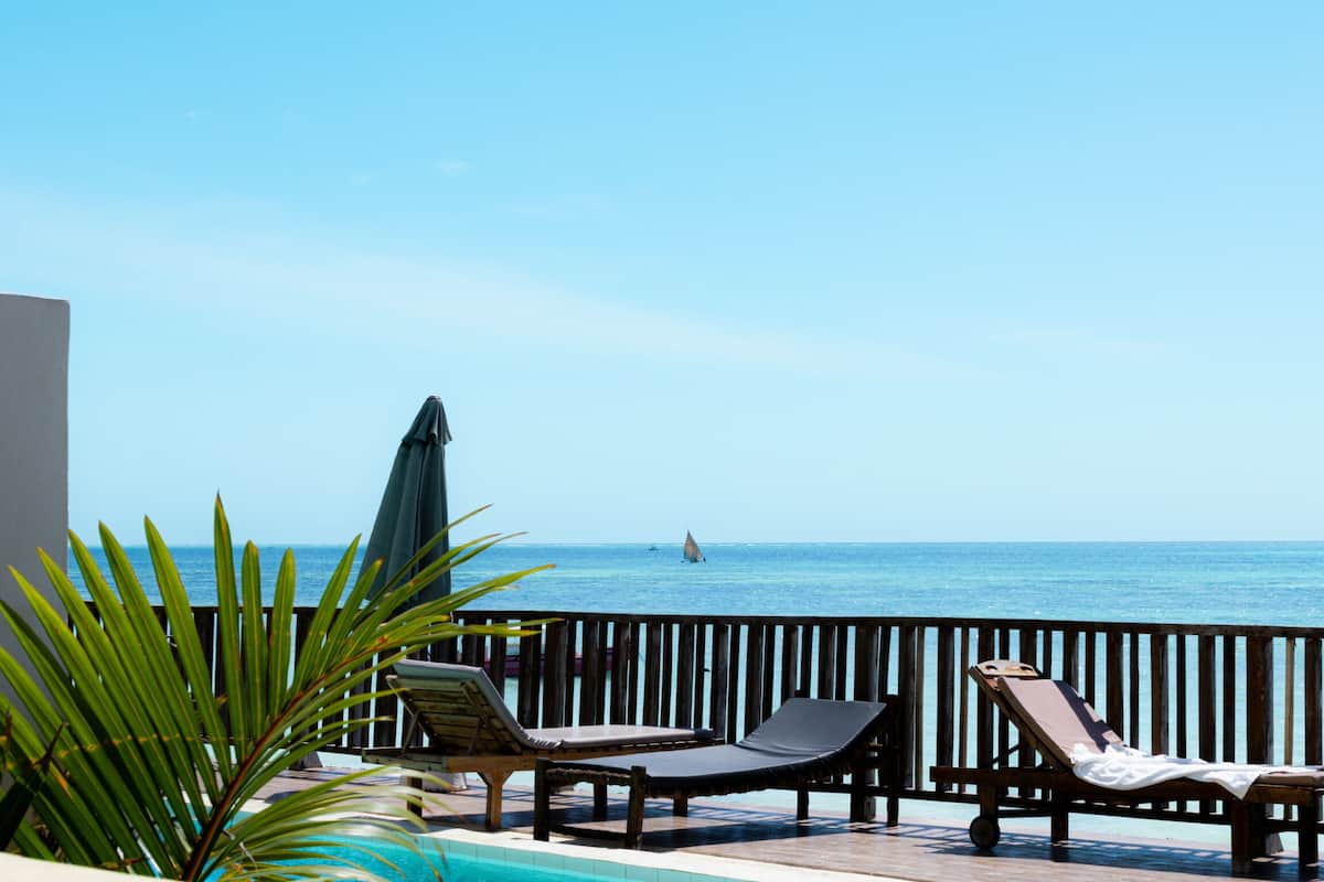 Zona de piscina con sillones reclinables y una sombrilla, con vista al mar.