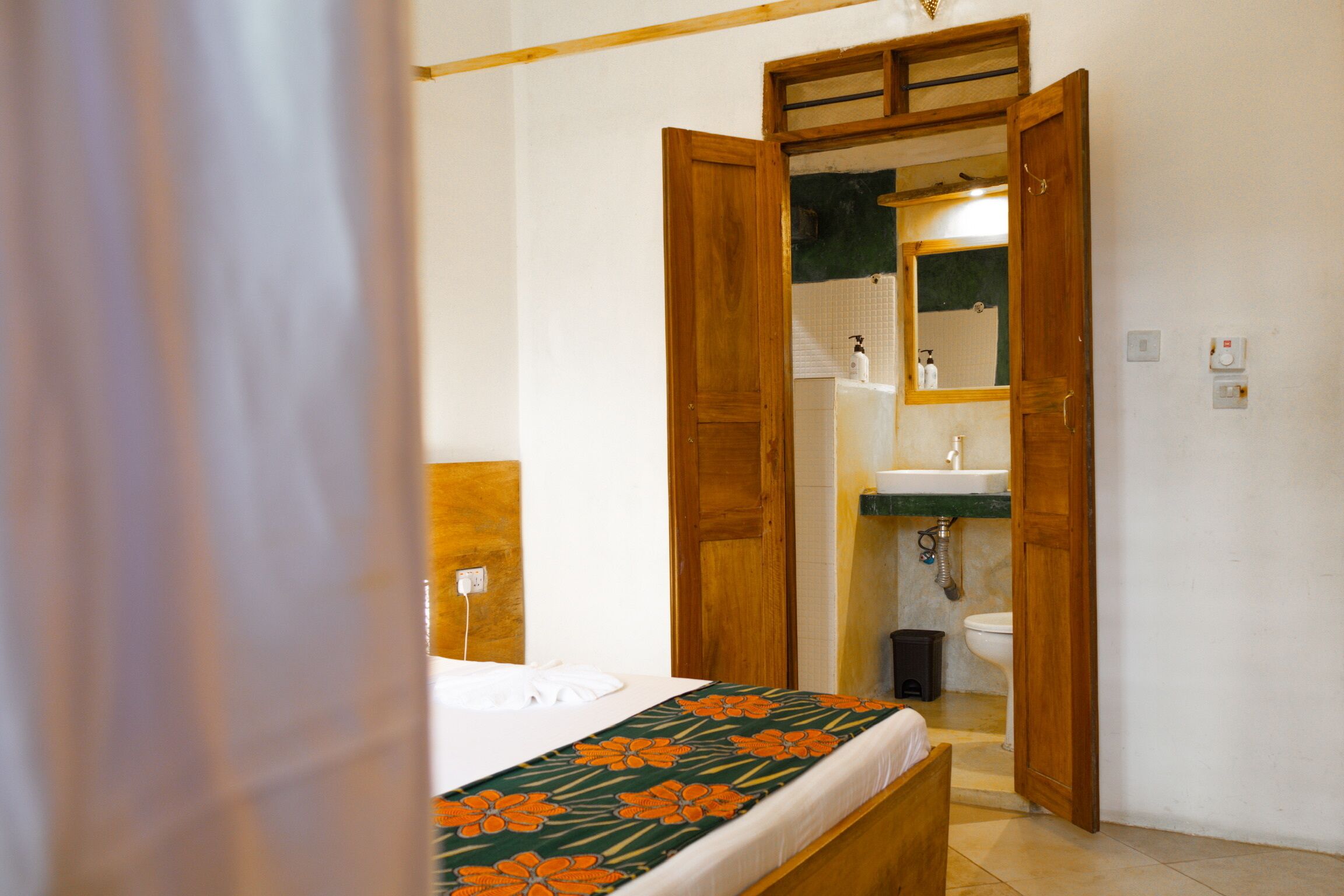 A bedroom with a bed, wooden door, and a bathroom visible through an open door.