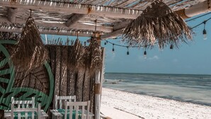A beachside lounge with a thatched roof, white chairs, and a wooden deck overlooking the ocean. - Pili Pili House (Jambiani)