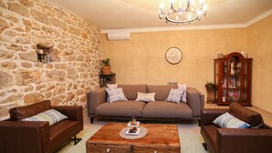 A living room with a stone wall, a brown sofa set, a wooden coffee table, and a chandelier. - Stunning Villa Bozini Dvori (Sveti Filip i Jakov)
