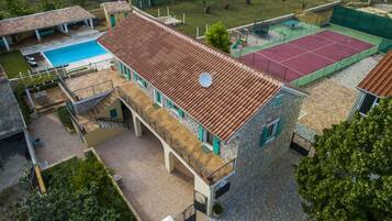 A two-story building with a tiled roof, a swimming pool, and a tennis court.