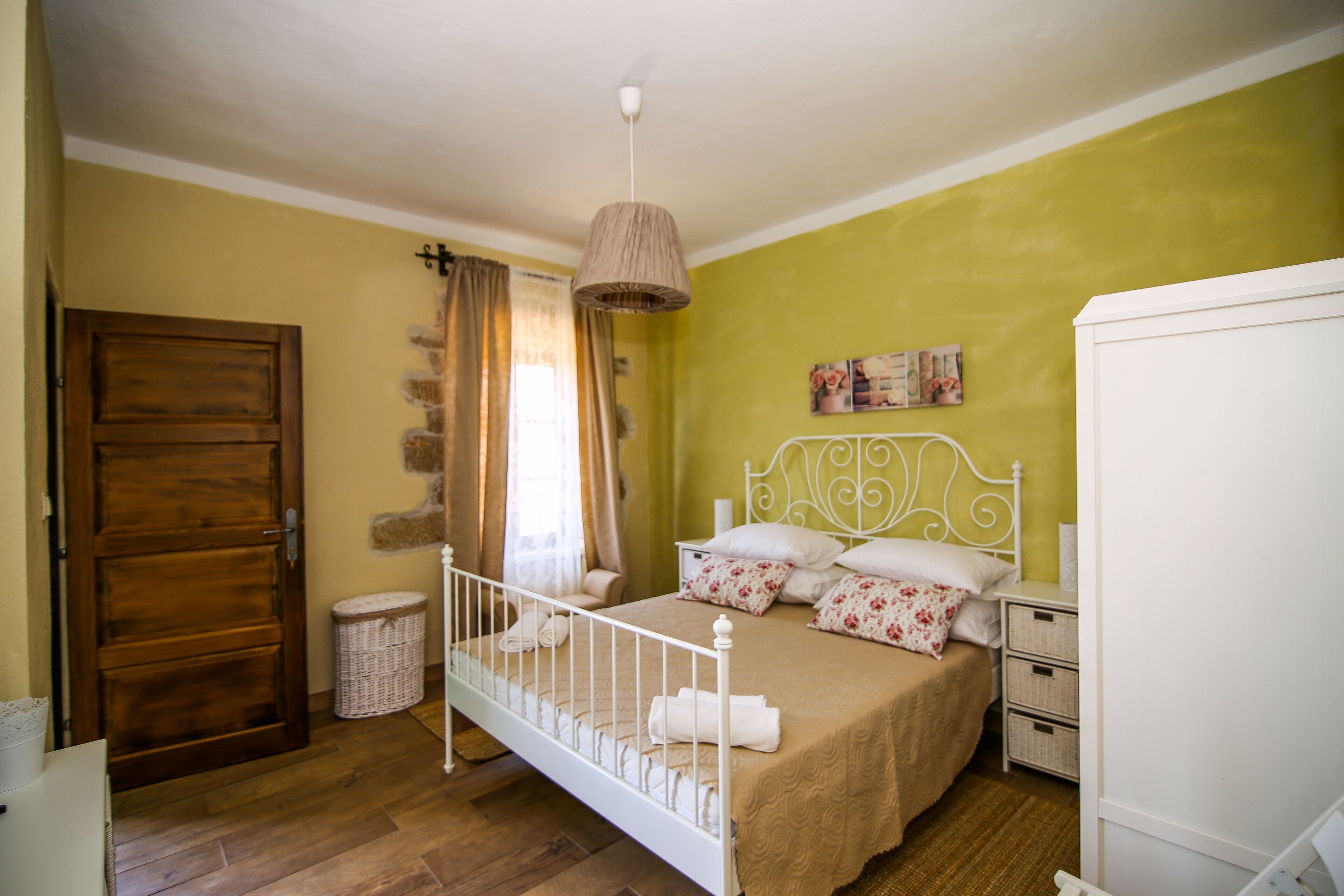 Een slaapkamer met een houten deur, een bed met een wit metalen frame, een hanglamp en een groene wand.